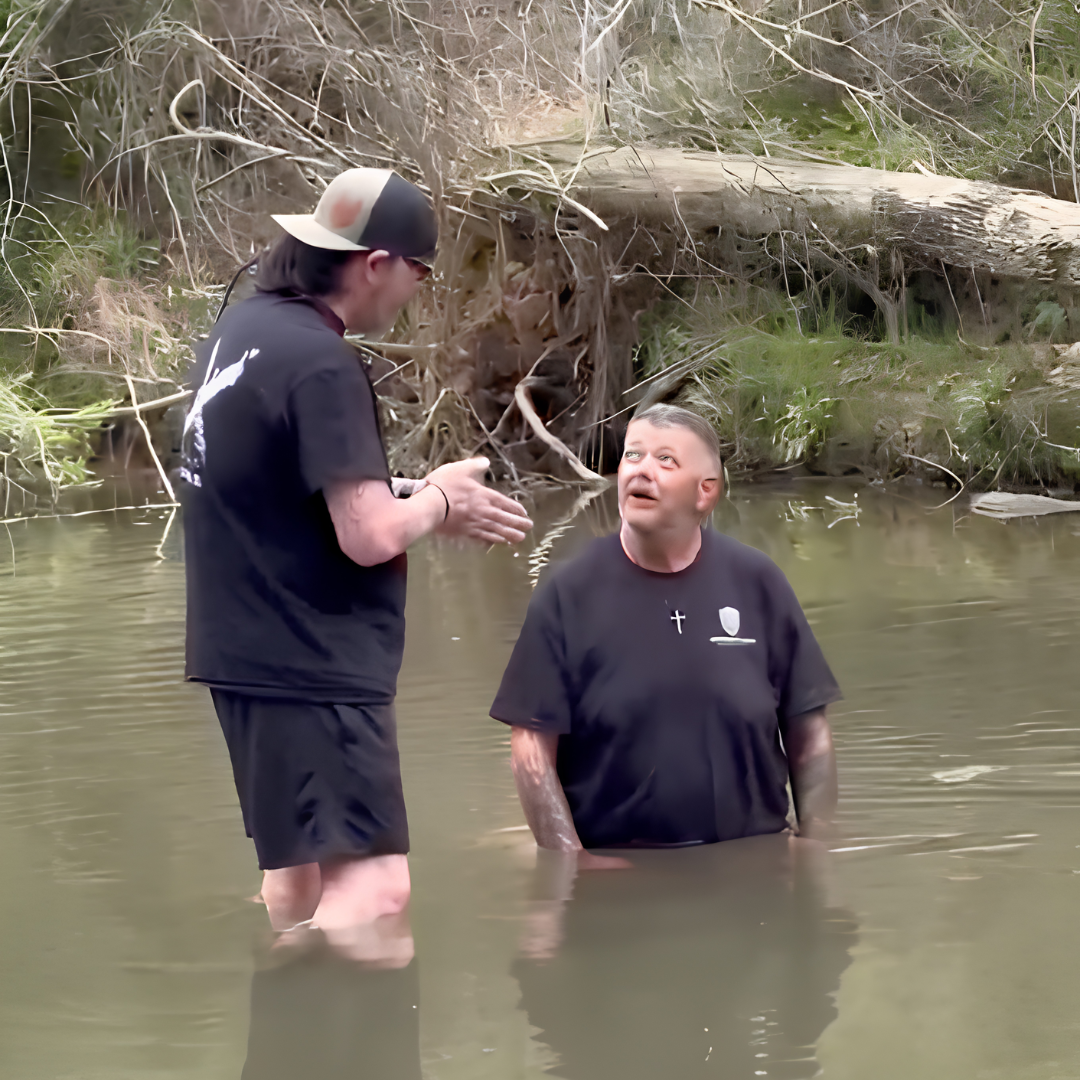 Two men standing in a river with trees and fallen logs in the background